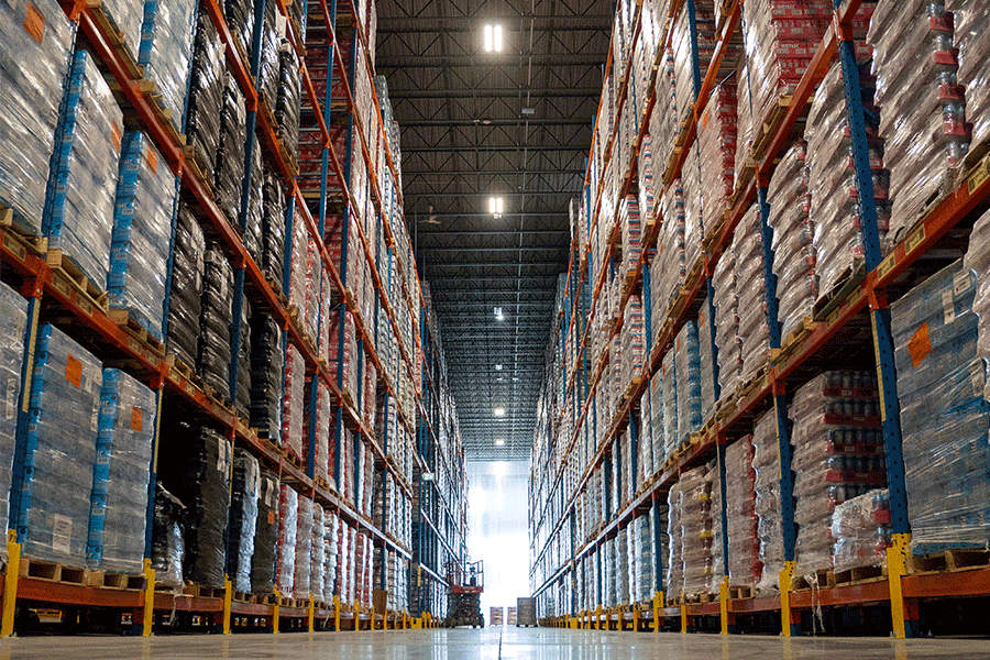 Low-angle perspective looking down a tall warehouse aisle filled on both sides with palletized inventory stored on blue and orange double-deep pallet racking.