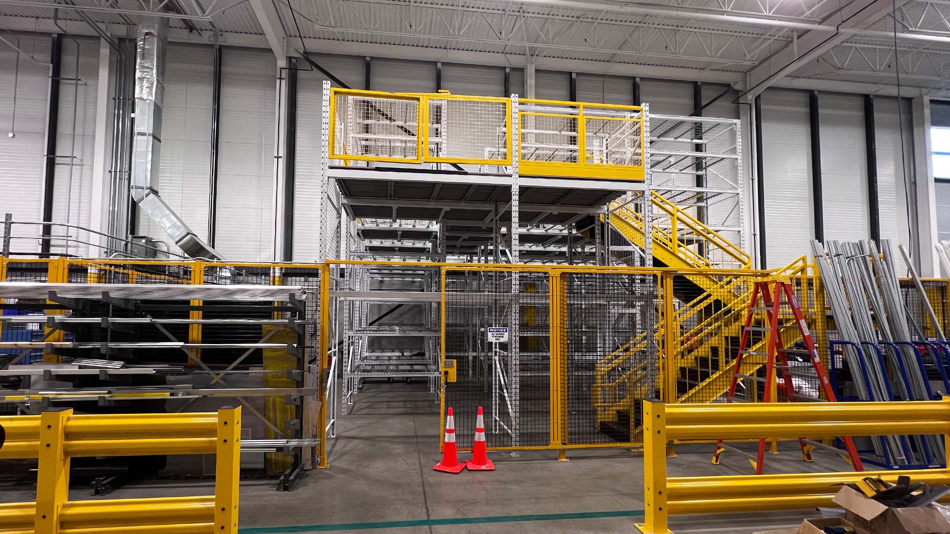 Front view of a multi-tier industrial pick tower structure with yellow safety fencing, access stairs, and protective floor guardrails.