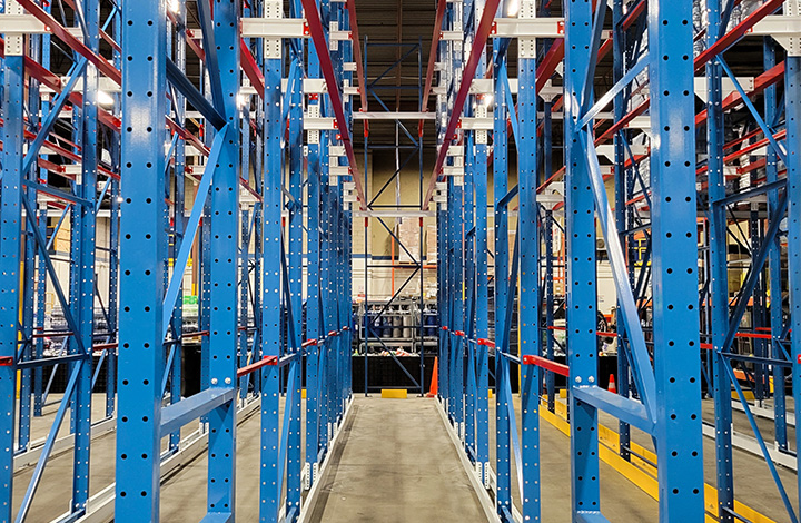 Eye-level view looking into an empty bay of a blue drive-in pallet racking system with red support rails and white floor guides.