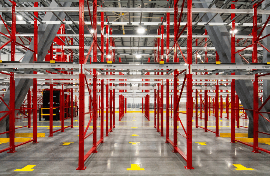 Front-facing view of a large red pushback pallet racking system installed in a high-ceiling warehouse with grey structural columns and floor marking guides.
