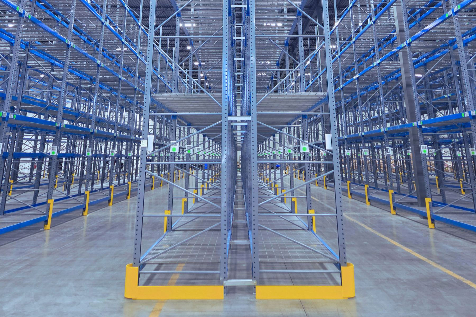 Down-the-aisle view of a selective pallet racking installation showing wire mesh shelf decking and column guards inside an automotive distribution center.