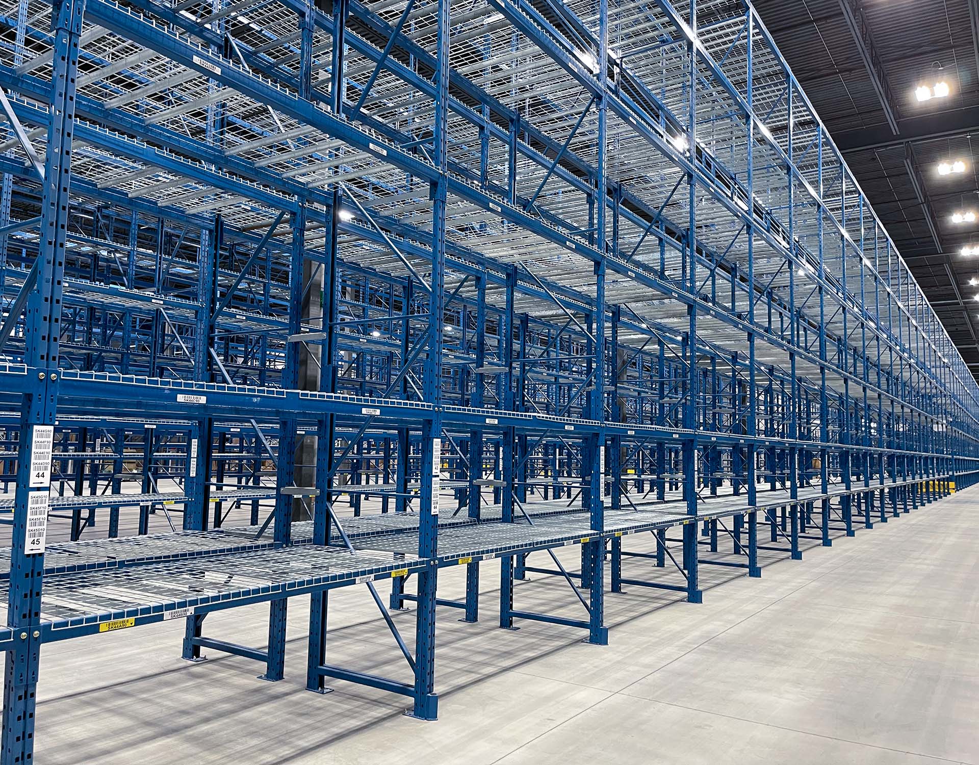 Angle-shot looking down a long run of blue selective pallet racking with wire mesh decking and location labels on the beam faces.