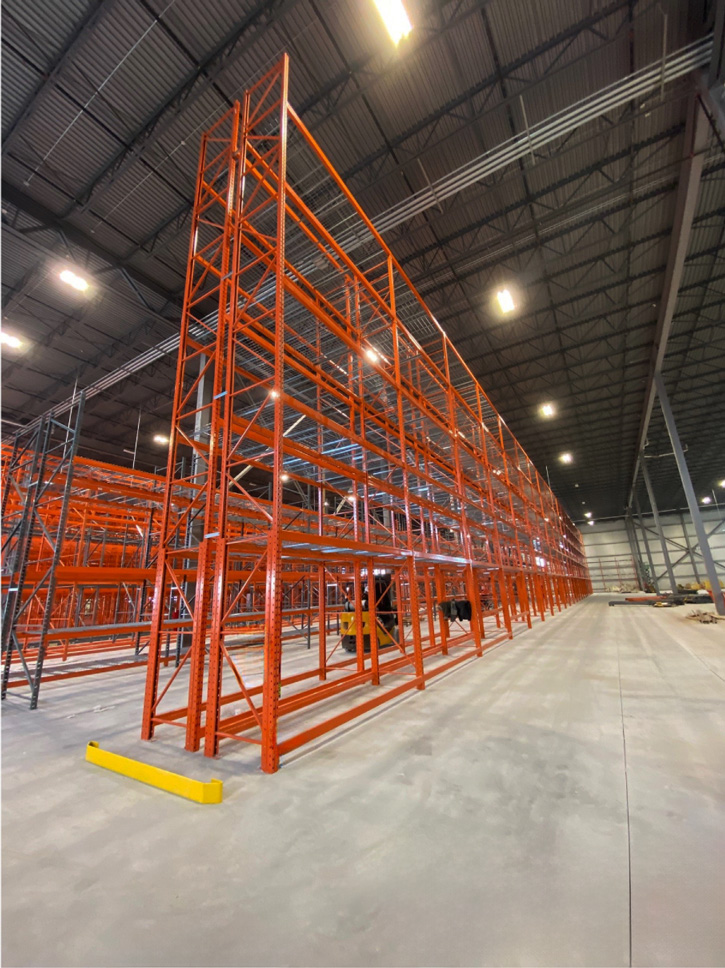 Wide-angle view showing the full height of a tall orange VNA selective pallet racking bay with a yellow floor end-guard in an empty facility.
