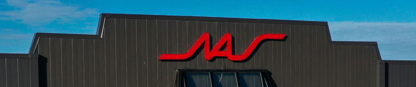 Close-up view of the red NAS company logo mounted on the exterior dark metal siding of the head office building against a blue sky.