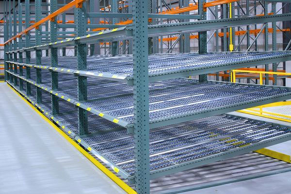 Side angle of multi-level grey carton flow shelf tracks mounted within structural steel racking frames.