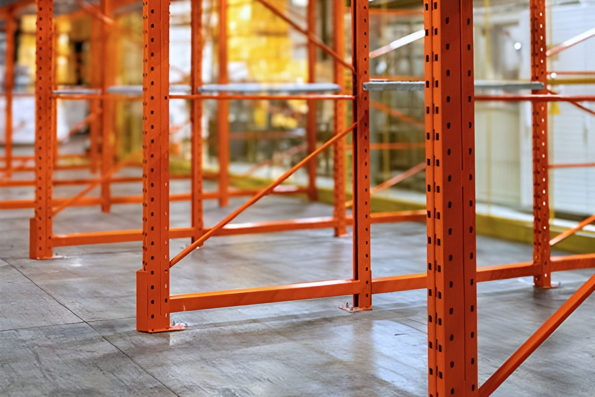 Ground-level view showing the base plates and support beams of an orange drive in warehouse racking solution.
