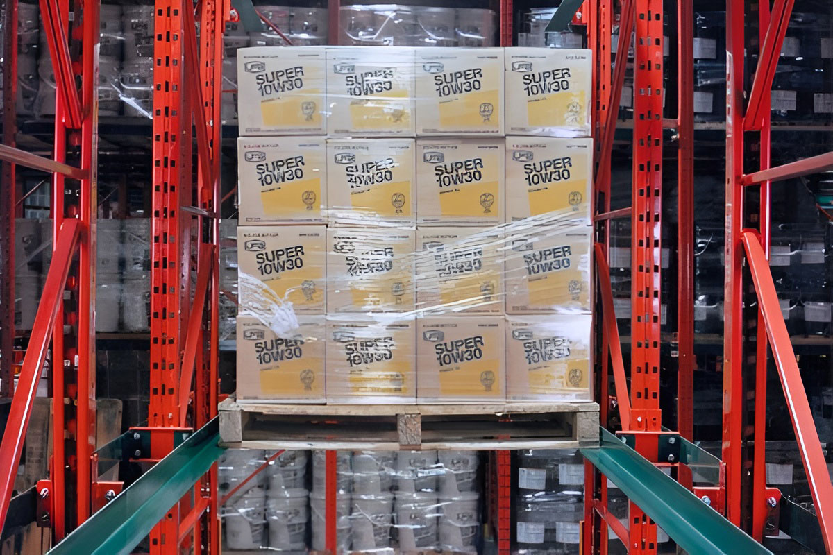 Close-up view of motor oil boxes on a wooden pallet resting on green support rails within an orange drive in rack structure.
