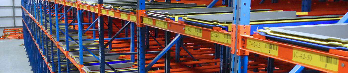 Elevated view of a multi-level pushback pallet racking system featuring nested sliding carts and yellow safety stops on orange structural beams and blue upright frames.
