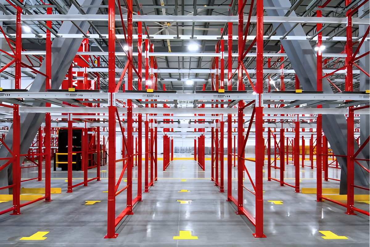 Front view of a red steel pushback warehouse racking solution showing empty bays and yellow floor guides in a distribution center.