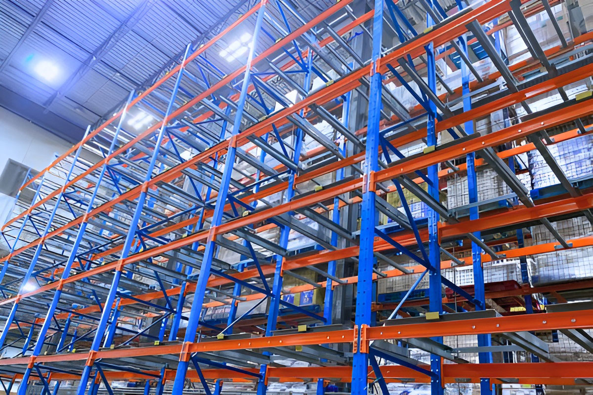 Low-angle view looking up at a multi-tier blue and orange pushback rack structure designed for high-density pallet storage.
