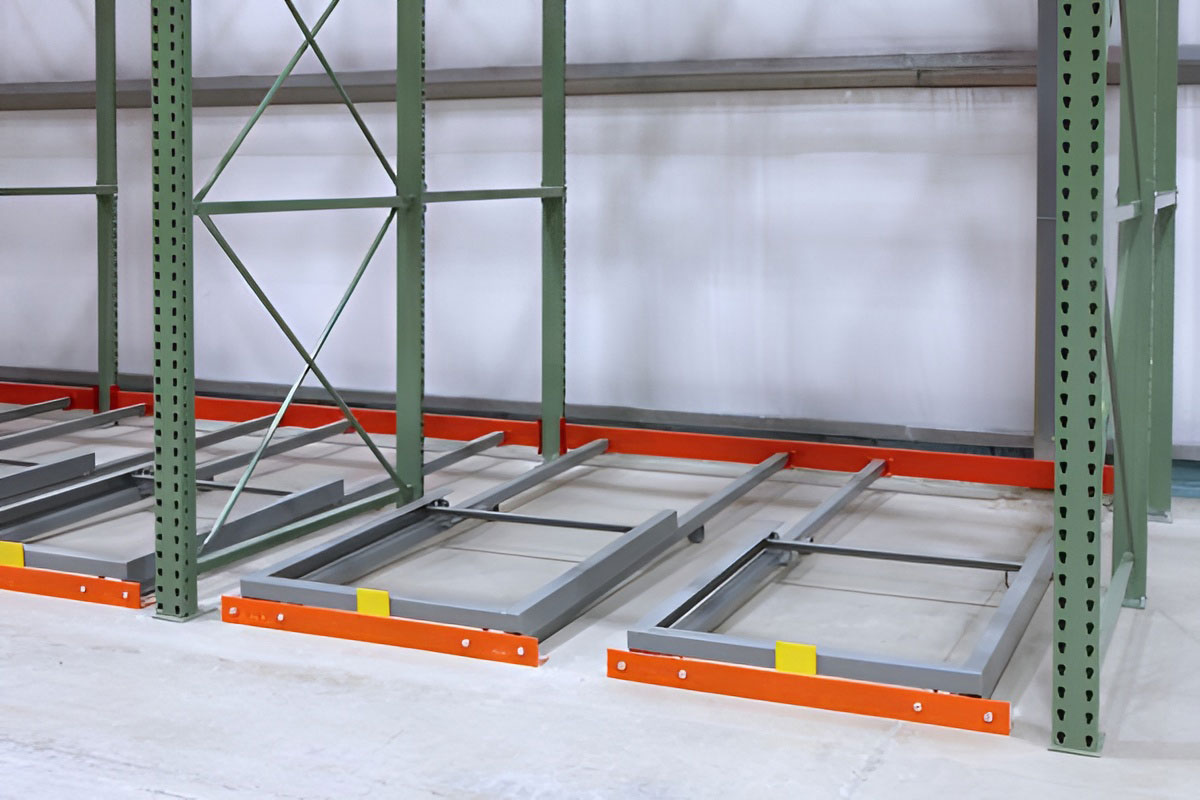 Ground-level view of grey pushback cart mechanisms resting on floor-mounted orange rails within green upright frames.