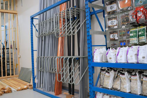 Store display rack integrating vertical pipe dividers for conduit and copper tubing alongside standard shelves for bagged construction materials.