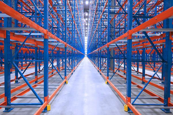 Ground-level perspective down a very narrow aisle (VNA) selective racking system showing yellow floor guide rails and orange crossbeams.