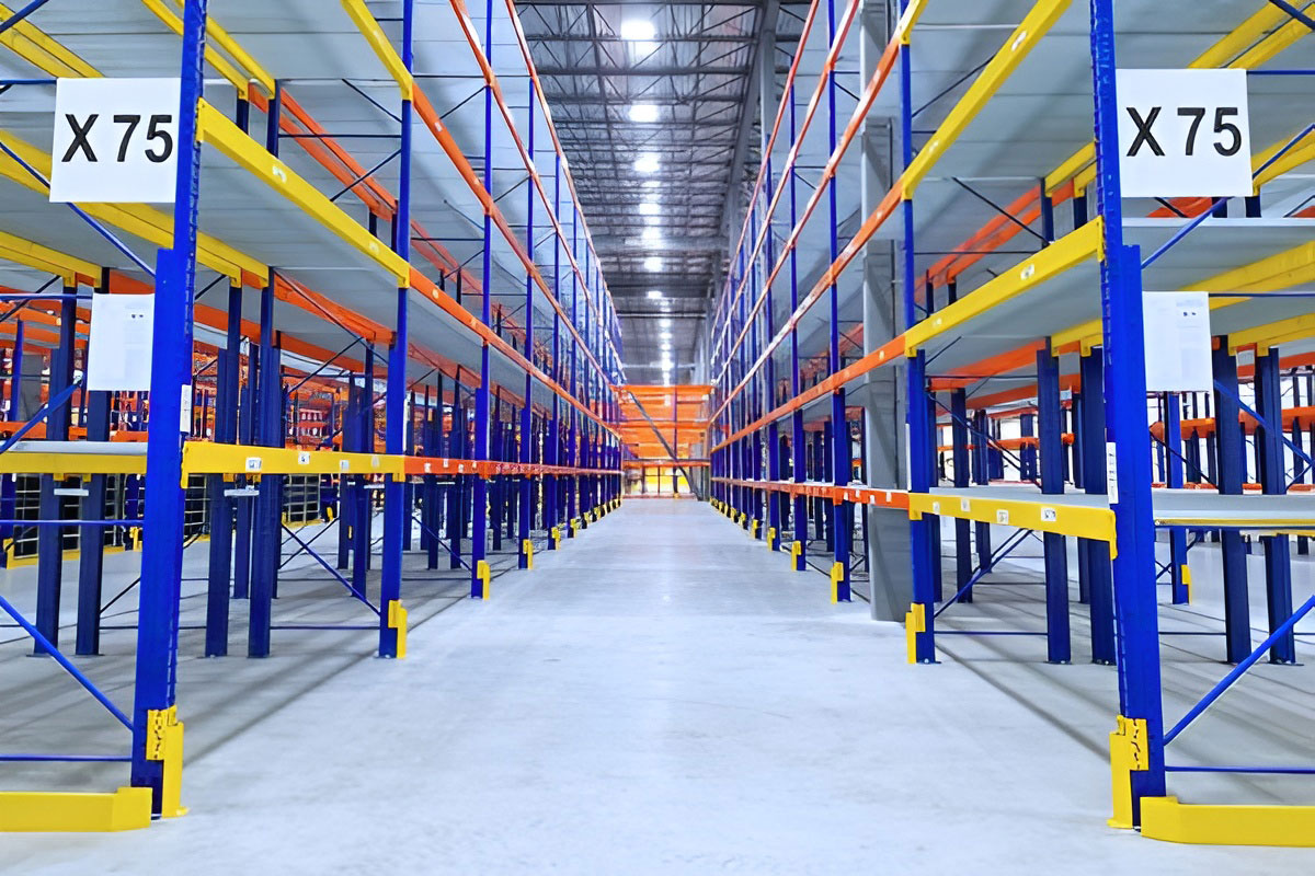 Wide aisle view between blue selective racking frames featuring yellow step beams, row protectors, and aisle location signs marked X75.