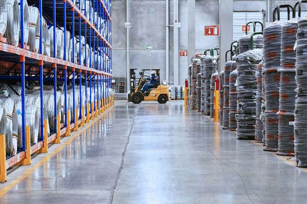 Forklift operator navigating a wide aisle past high-density pallet racks loaded with coiled industrial inventory.