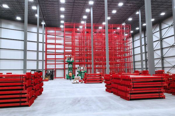 Industrial installation crew assembling a tall red pallet shuttle system in a high-bay warehouse facility.
