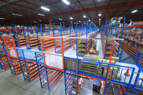 High-angle view of a warehouse mezzanine platform featuring blue safety handrails, orange sliding mesh gates, and integrated storage racking above and below.