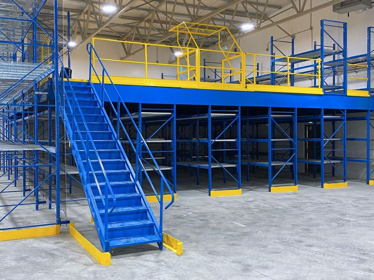Rack-supported mezzanine platform featuring a blue industrial access staircase, safety handrails, and open lower-level shelf storage.