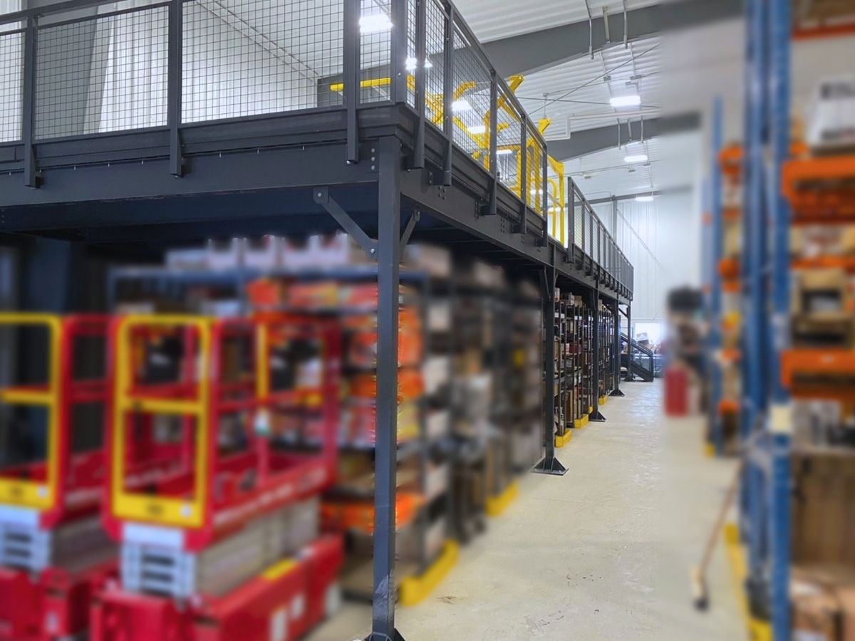 Free-standing structural mezzanine platform with mesh safety railings built over lower-level storage shelving and aisle space.